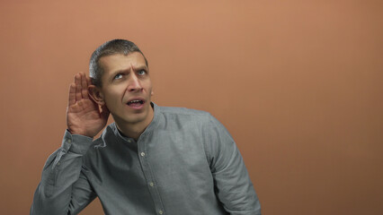 Man wearing gray shirt against a brown wall looking curious and attentive while listening intently...