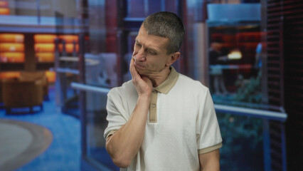 Man expressing pain indoors in a modern hotel lobby with his hand on his face showcasing discomfort...