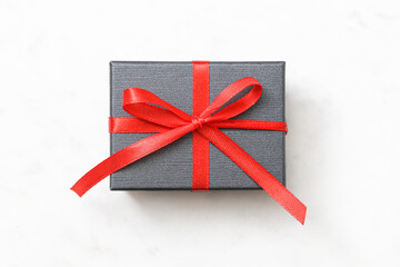 Elegant black gift box with red ribbon. Festive wrapping on white marble background. Holiday...