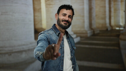 Man with beard makes a no gesture amidst ancient columns in rome, capturing a dynamic moment in the...