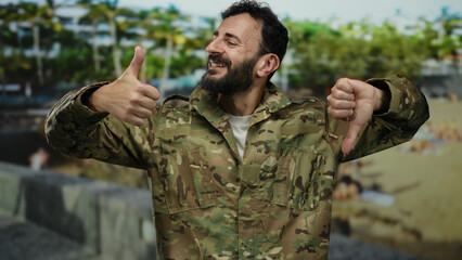 Military man with beard in camouflage uniform gestures thumbs up and down while standing in a green...