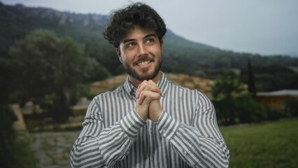 Young man with beard smiling in a green park displaying relaxed and happy demeanor wearing a...