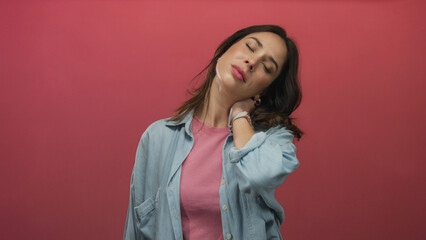 Woman in denim shirt on red background showing neck pain expression in isolated environment