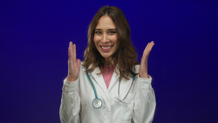Young hispanic female doctor wearing a stethoscope smiles confidently against a vibrant blue...