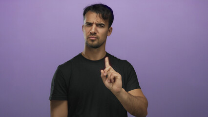 Young man in black shirt gesturing no with finger against isolated purple background conveying...