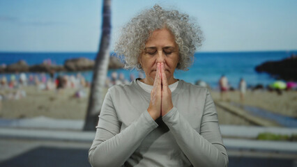 Woman with grey hair meditating on a beach with a serene sea background, embodying tranquility and...