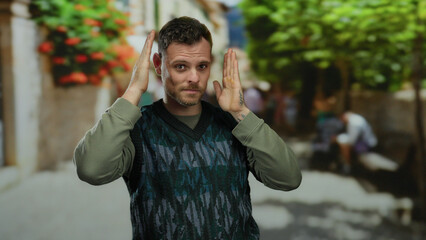 Young man making frame gesture outdoors in a vibrant urban street setting with trees and people in...