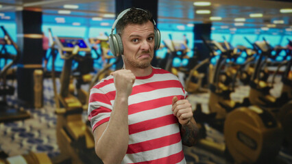 Young man with headphones making a fist in a gym with exercise machines blurred in the background...