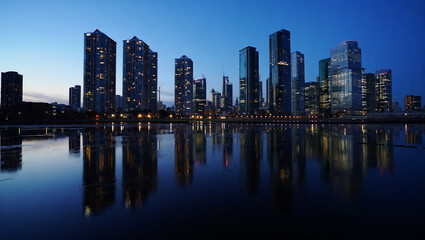 Obraz premium Illuminated skyscrapers reflected in dark water at dusk city skyline modern architecture