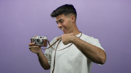 Smiling man holding vintage camera points towards viewer against purple background showcasing...