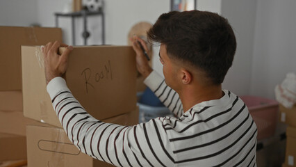 Young man in striped shirt labels cardboard boxes in his new apartment during a home move, reflecting a fresh start and personal organization in the cozy indoor setting.