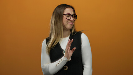 Woman with glasses showing a rejection gesture against an orange background in an isolated setting,...