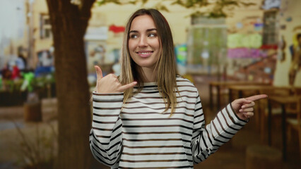 Obraz premium Woman gesturing phone and pointing on urban street outdoors showcasing casual style with vibrant, expressive attitude.