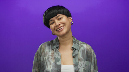 Young chinese woman playfully sticking out tongue against isolated purple background, expressing...