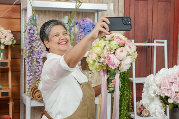 Happy senior asian florist taking selfie with bouquet inside flower shop promoting flower product online cheerful moment showing modern way of digital marketing for small floral business