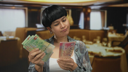 Woman examines hong kong banknotes inside a cozy restaurant, showcasing thoughtful expression in a...