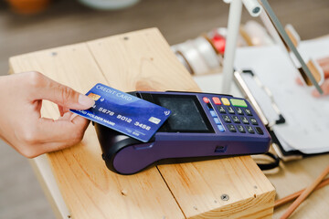 Hand inserting credit card into reader on wooden counter inside flower shop run by asian senior female florist managing small floral business after retirement