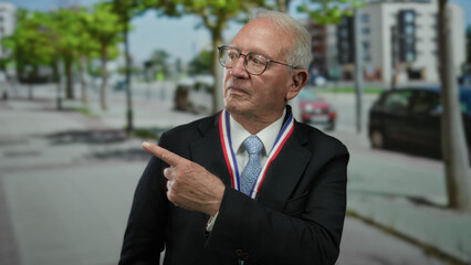 Senior man in suit with medal pointing on urban street with cars and trees in background...