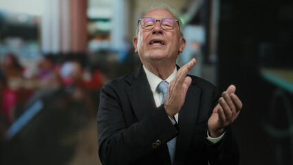Senior man in a suit clapping joyfully at an outdoor restaurant terrace, capturing a lively street...
