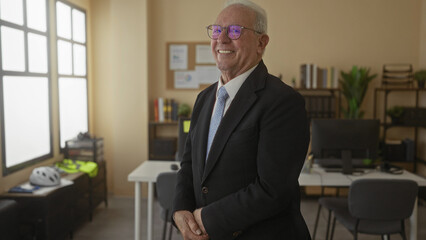 Senior man smiling in business suit standing confidently in modern office interior with desks,...