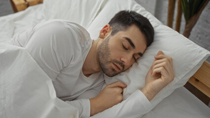 Young man sleeping peacefully in bed with white sheets in a cozy bedroom, highlighting tranquility...
