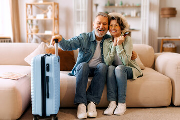 Joyful European senior spouses posing with packed luggage and travel tickets, ready for vacation...