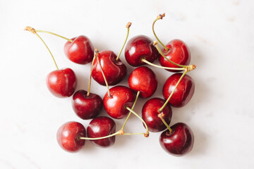 Fresh ripe cherries on marble background. Juicy red fruit with green stems arranged in flat lay. Minimalist healthy snack concept. Natural organic dessert ingredient. Sweet seasonal summer harvest.