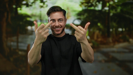 Young man with beard in park making rude gesture with both middle fingers raised, surrounded by...