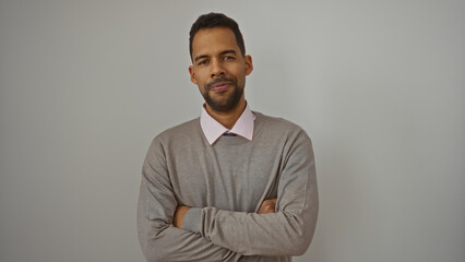 Young hispanic man standing confidently with arms crossed isolated against white background, exuding charm and confidence in a relaxed casual attire with neutral expression.