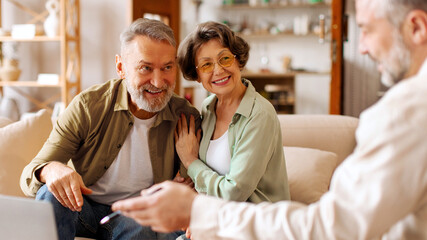 Male realtor consulting senior couple buyers showing project on laptop, man and woman clients buy...