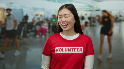 Woman smiling in an airport terminal wearing volunteer shirt with blurred travelers in background,...