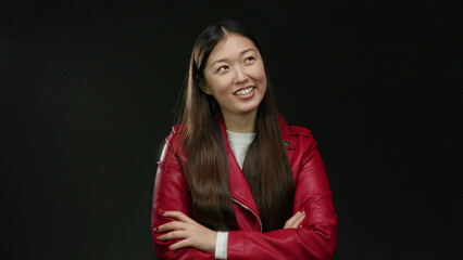 Woman smiling confidently in red jacket against dark background, exuding beauty and style with crossed arms, showcasing modern elegance and self-assurance.
