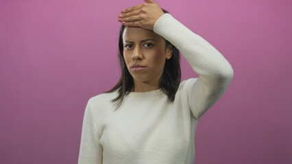 Woman covering face with hand in front of pink wall showing emotion and isolation in studio setting