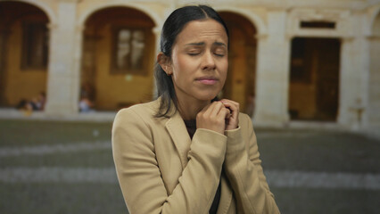 Fototapeta premium Woman in jacket looks worried in historic town square with arches in background, conveying emotion and narrative against old architecture.