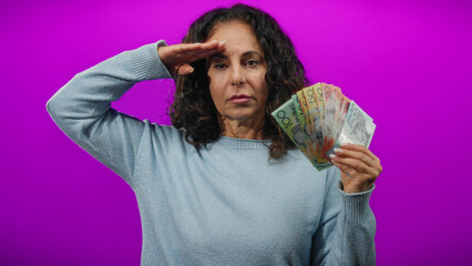 Woman holding australian dollars in front of a vibrant purple wall, demonstrating financial...