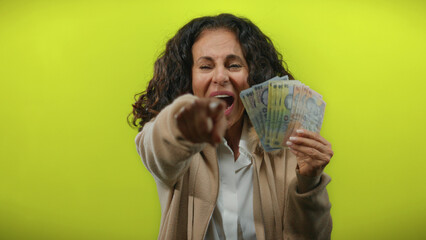 Woman holding romanian banknotes excitedly on a vibrant yellow background, pointing forward...