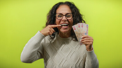 Middle-aged woman from uae points at teeth while holding dirham banknotes against an isolated...