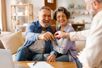 Realtor giving senior couple key to new house at meeting, owners making purchase deal, family...