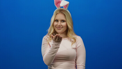 Woman wearing bunny ears sends a playful kiss against a vibrant blue background, showcasing a fun,...