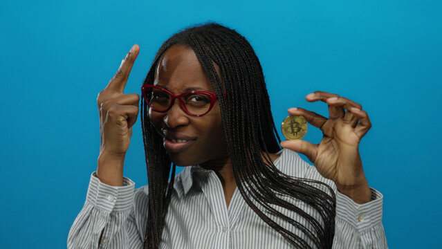 Woman holding bitcoin with confident gesture against isolated blue background, showcasing modern finance and cryptocurrency trends.