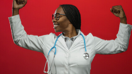 Confident female doctor smiling in lab coat with stethoscope posing against red background...