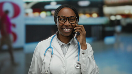 Woman smiling in a white coat with stethoscope talking on smartphone in indoor airport setting suggesting professional communication and travel theme. © Krakenimages.com