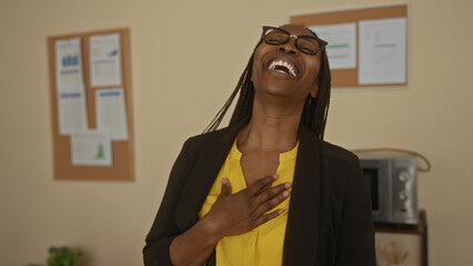 Woman smiling indoors in office setting wearing yellow top and glasses, exuding positive...