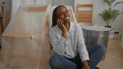 Woman smiling on phone in living room surrounded by unpacked furniture in new home showcasing happiness and modern lifestyle.