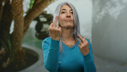 Woman with grey hair making an offensive gesture in a street outdoor setting showing defiance and...