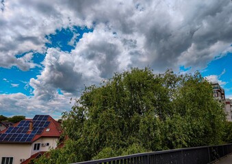 A tree with a lot of leaves is in front of a building. The sky is cloudy and the sun is shining through the clouds