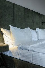 Close-up of modern hotel room interior with white pillows, clean bed, soft headboard and nightstand...