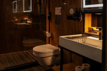 Modern hotel bathroom interior with white sink, toilet, glass shower cabin, illuminated mirror and...