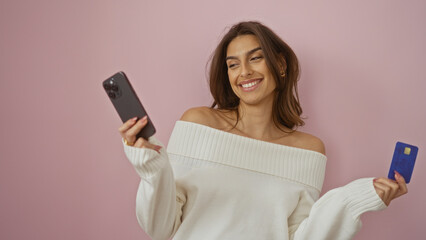 Naklejka premium Woman smiling holding phone and credit card against pink background showing happiness and modern lifestyle with attractive female figure isolated over simple backdrop.
