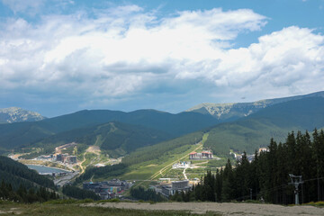 Scenic view of mountain resort with forests, hills and cloudy sky. Buildings and ski slopes visible...